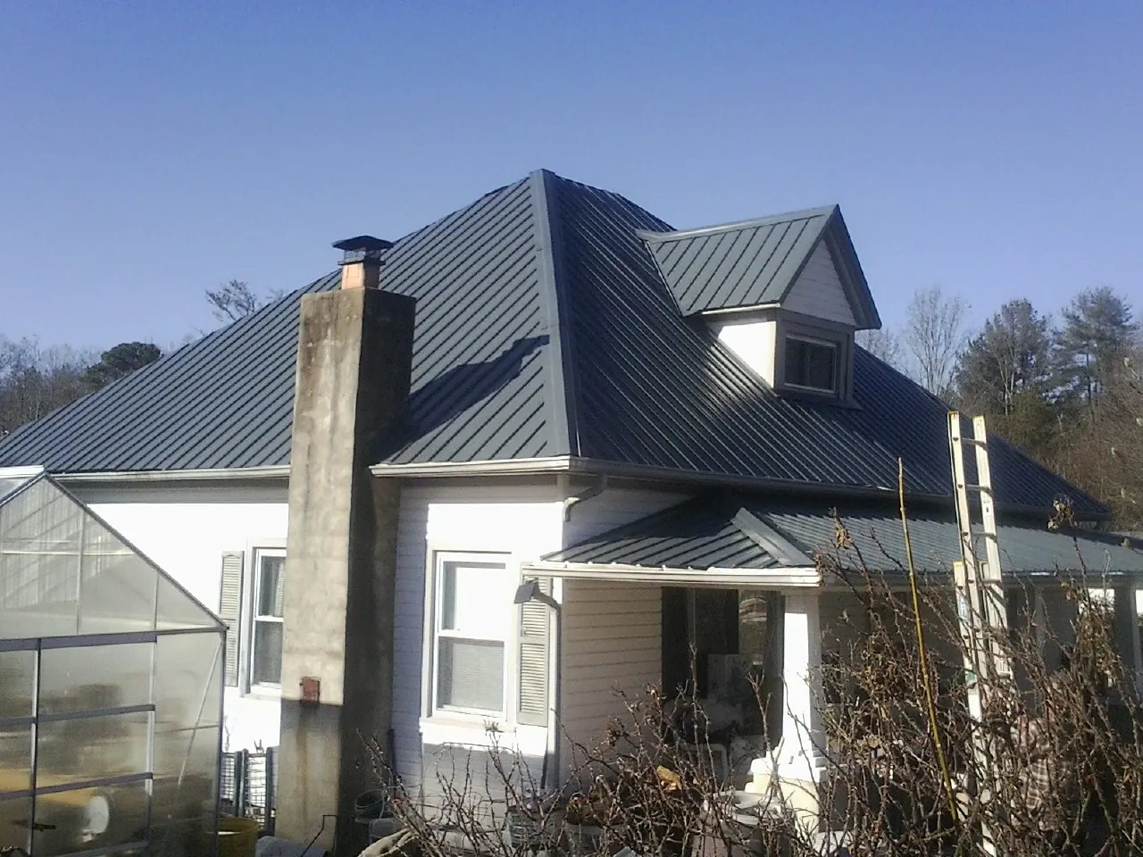 Dark blue standing seam metal roof on a white farmhouse with dormer — Slate & Tile Roof Repair by Roofing Brothers in Delton