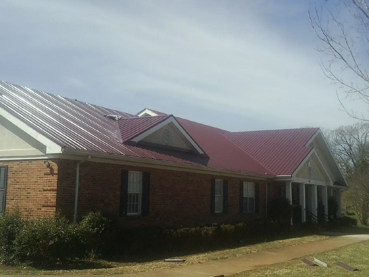 Red metal roof with gabled entries on a long brick building, from a Hail Damage Roof Repair job in Delton