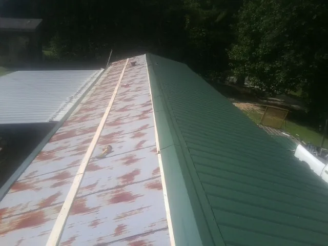 Old rusted panels beside newly installed green metal roofing — Wind Damage Roof Repair by Roofing Brothers in Delton