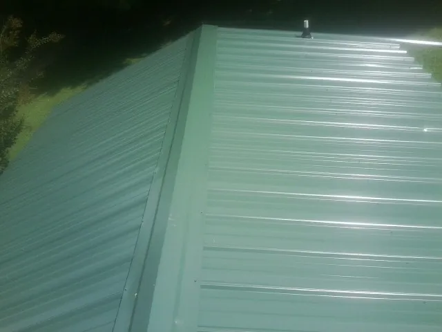 New green metal panels meeting at the ridge of a roof — Flat Roof Repair work by our crew in Delton