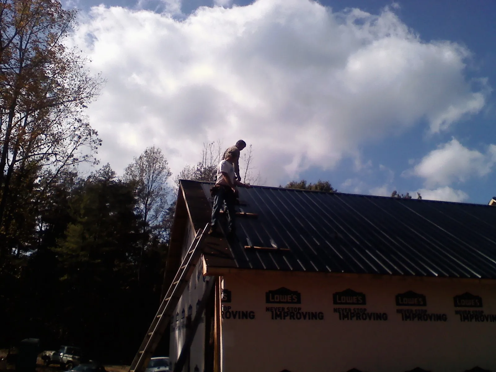 Roofer fastening dark metal panels high against a cloudy sky, from a Roof Inspection job in Delton