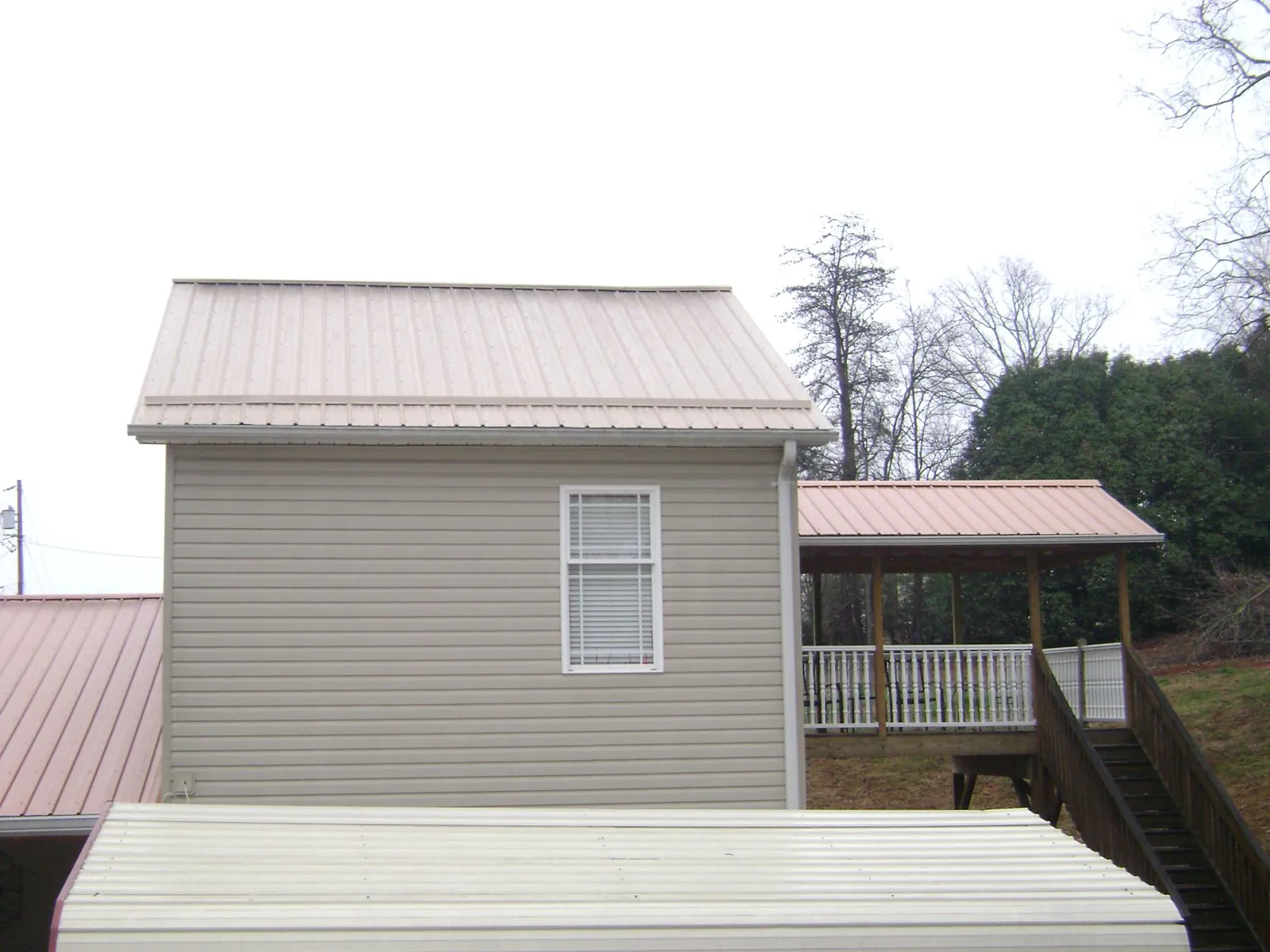 Tan metal roofs on a two story addition and attached porch, from a Roof Replacement job in Delton