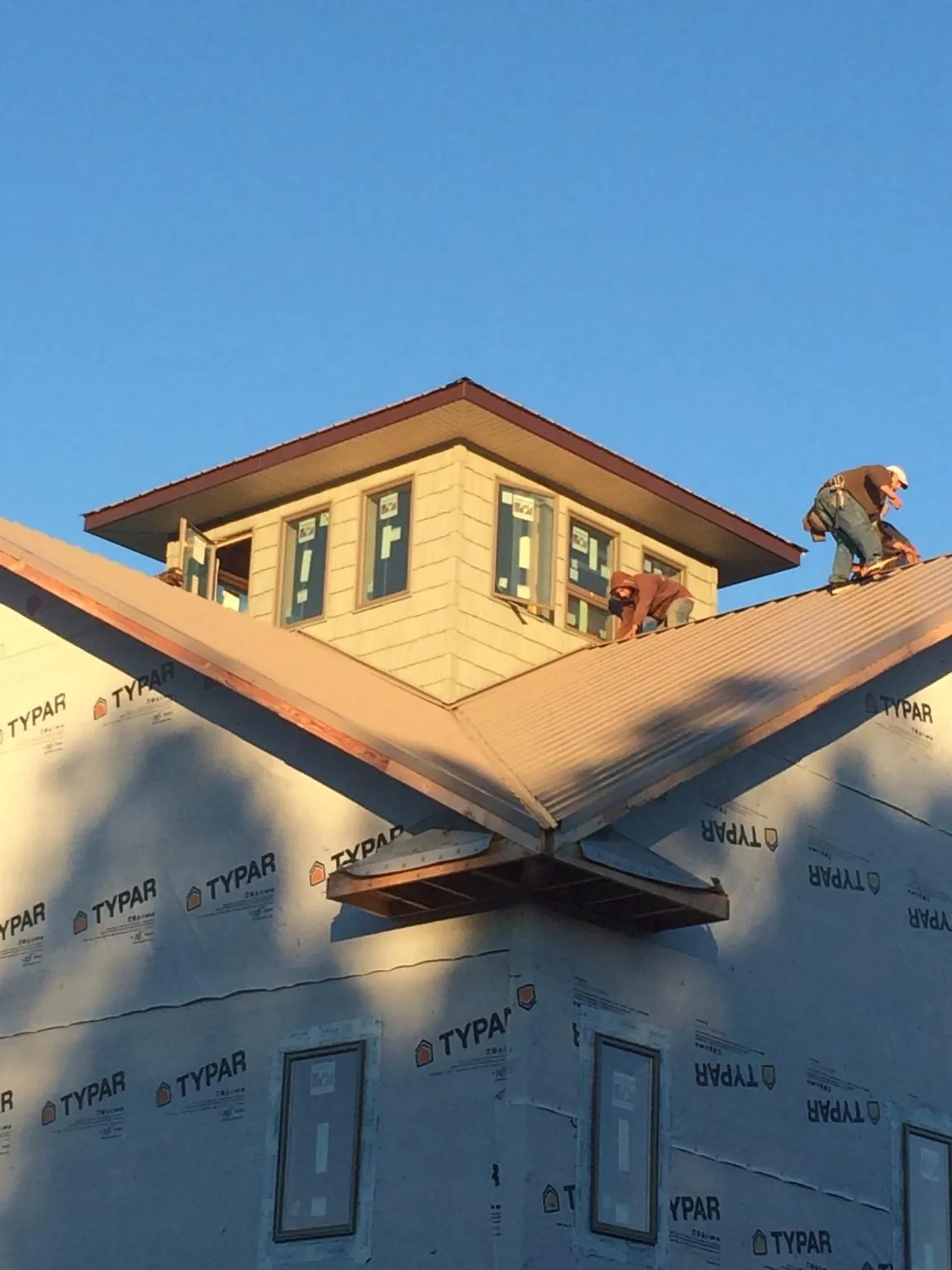 Roofers working around a rooftop cupola on a new metal roof at sunset — Roof Waterproofing in Delton by Roofing Brothers